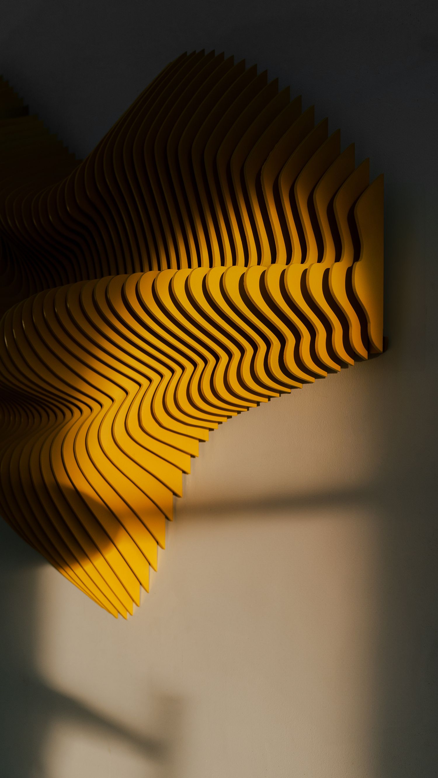 Close-up of yellow wavelike sculptural pattern creating dramatic shadows on wall.