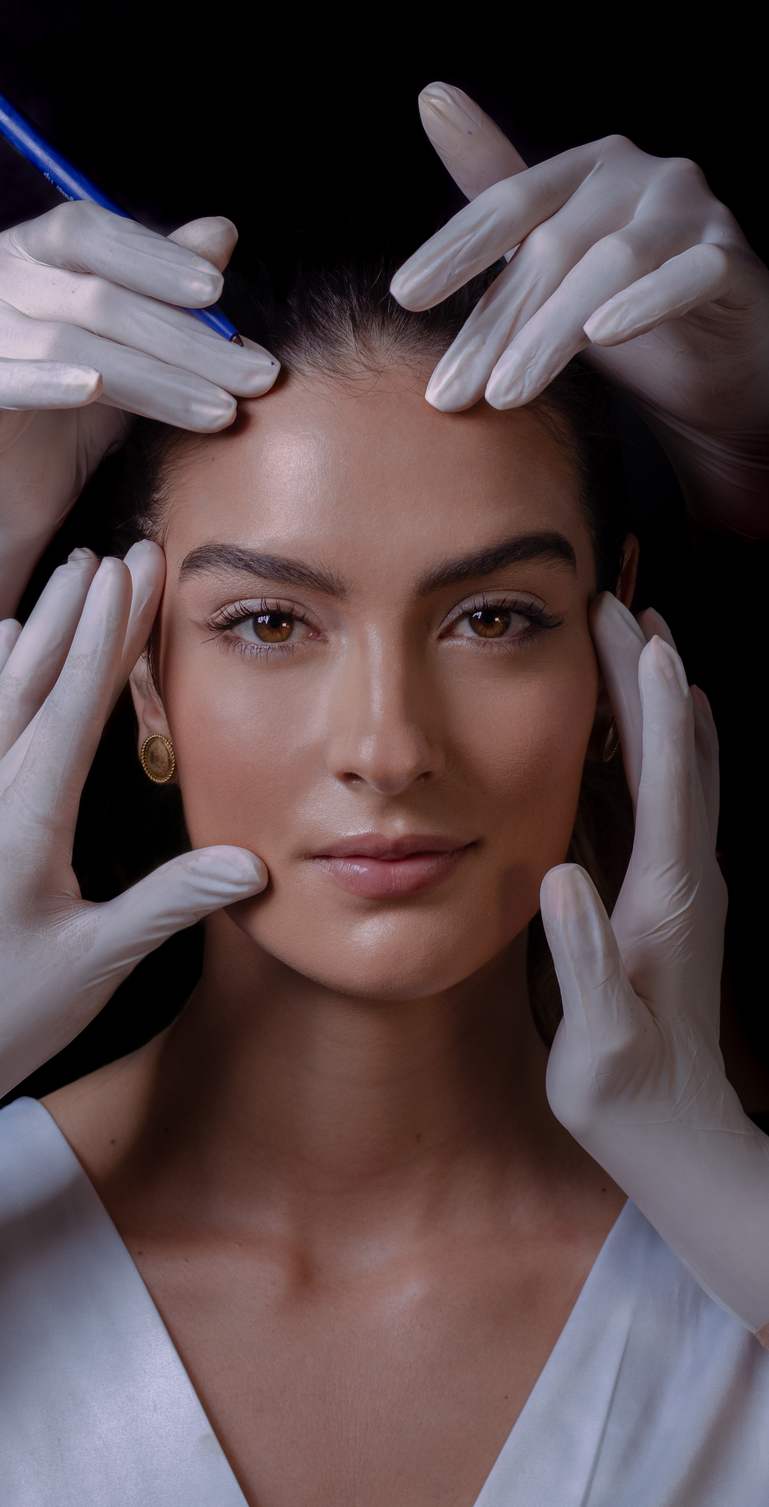 Artistic beauty shot with white gloved hands framing subject's face against dark background.
