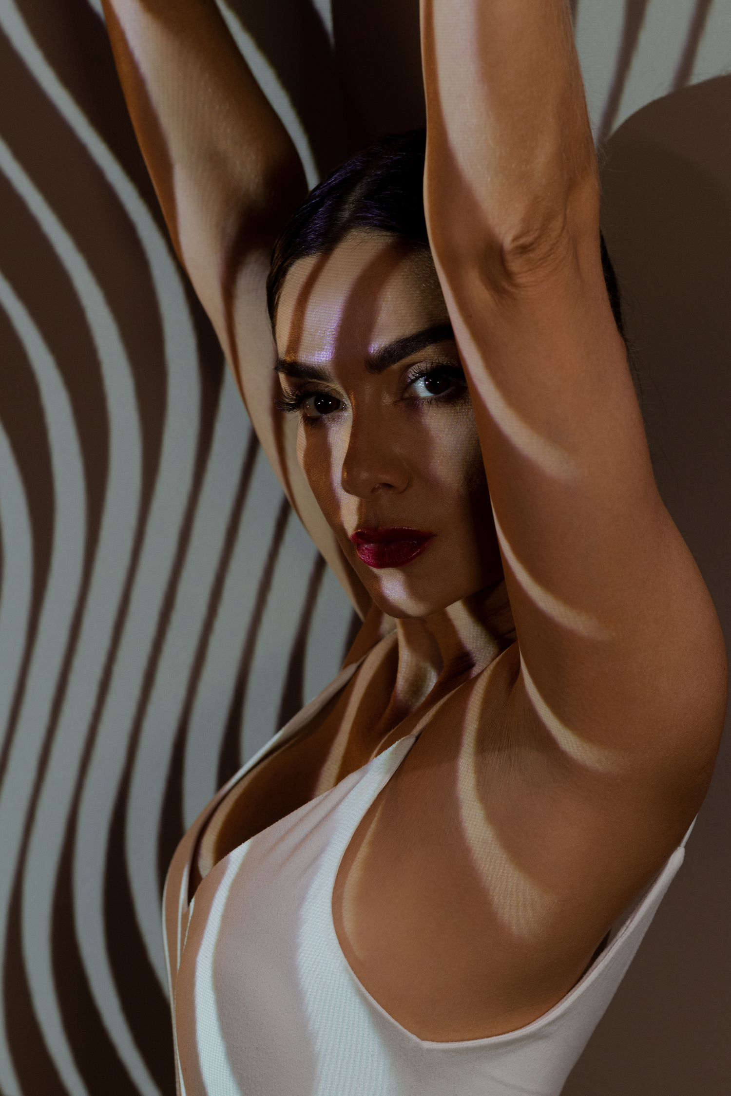 Fashion portrait with model in white tank top against curved stripe pattern background.