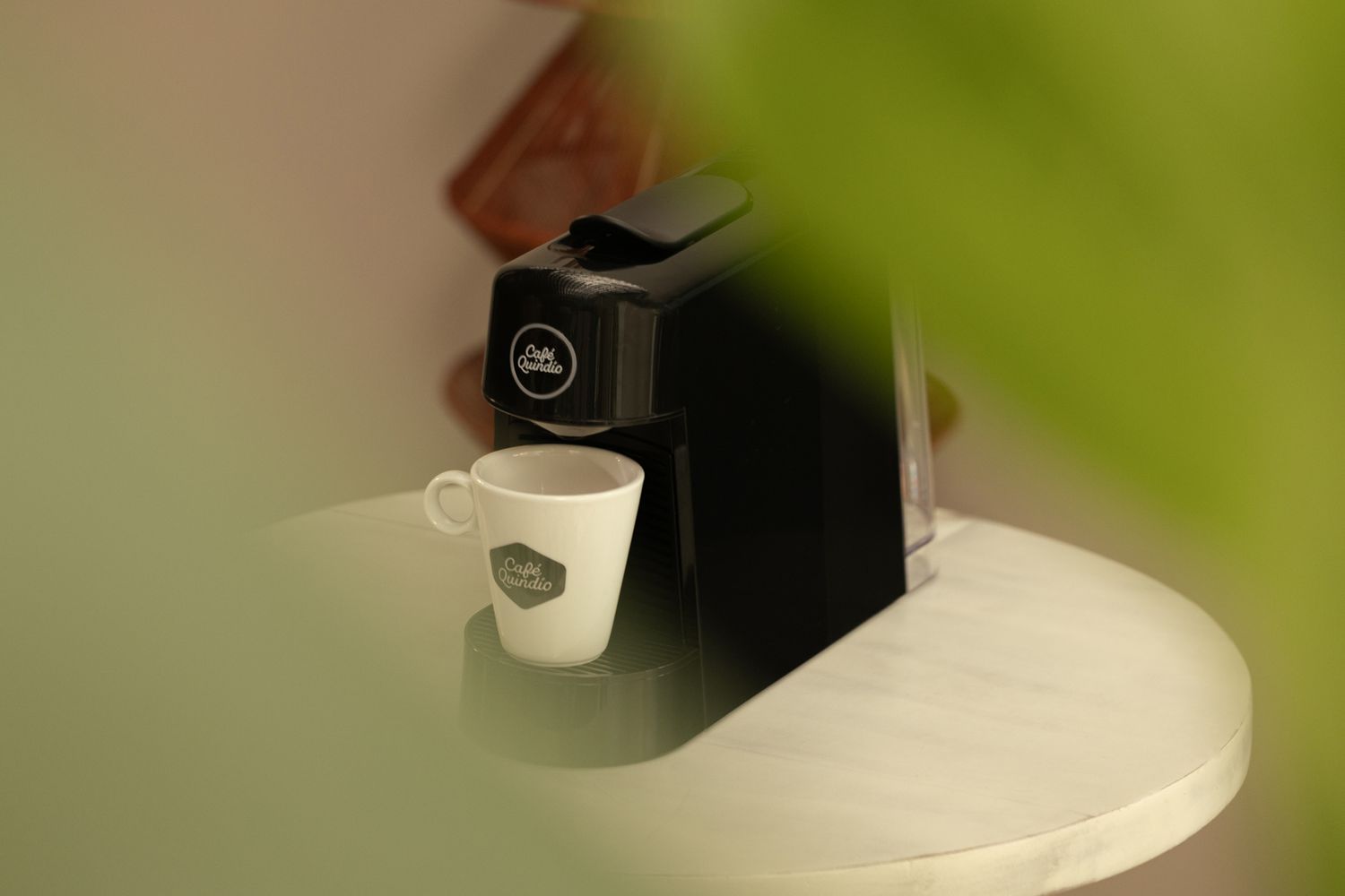 Close-up of coffee machine dispensing into white cup with plant leaf in frame.