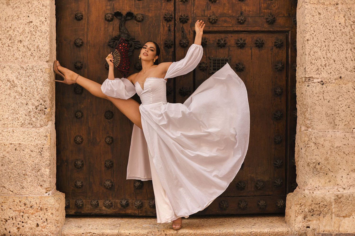Dancer in flowing white dress performs graceful pose against ornate wooden door.