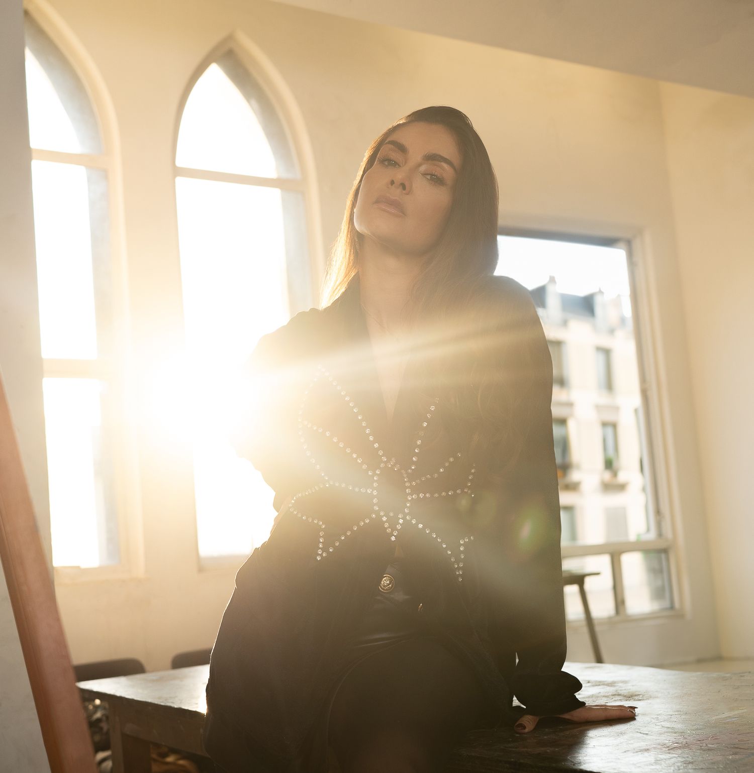 Sunlit interior with arched windows and person in dark clothing seated in bright natural light.