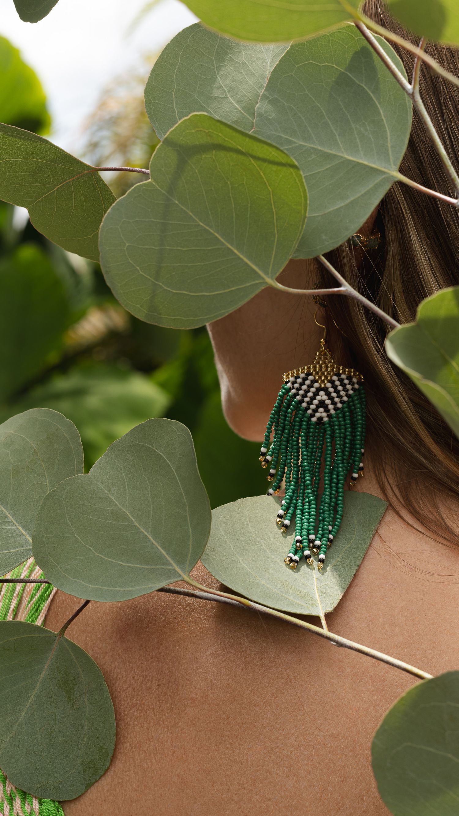 Round green leaves frame a detailed emerald and gold beaded statement earring.