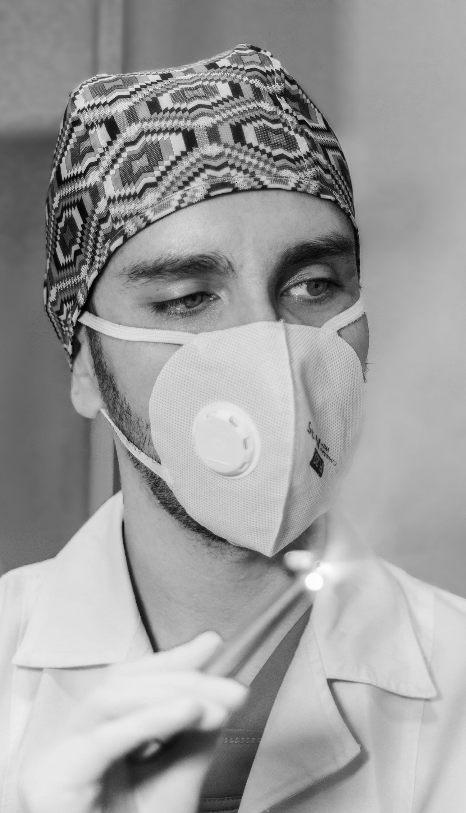 Healthcare worker wearing patterned surgical cap and protective mask in clinical setting.