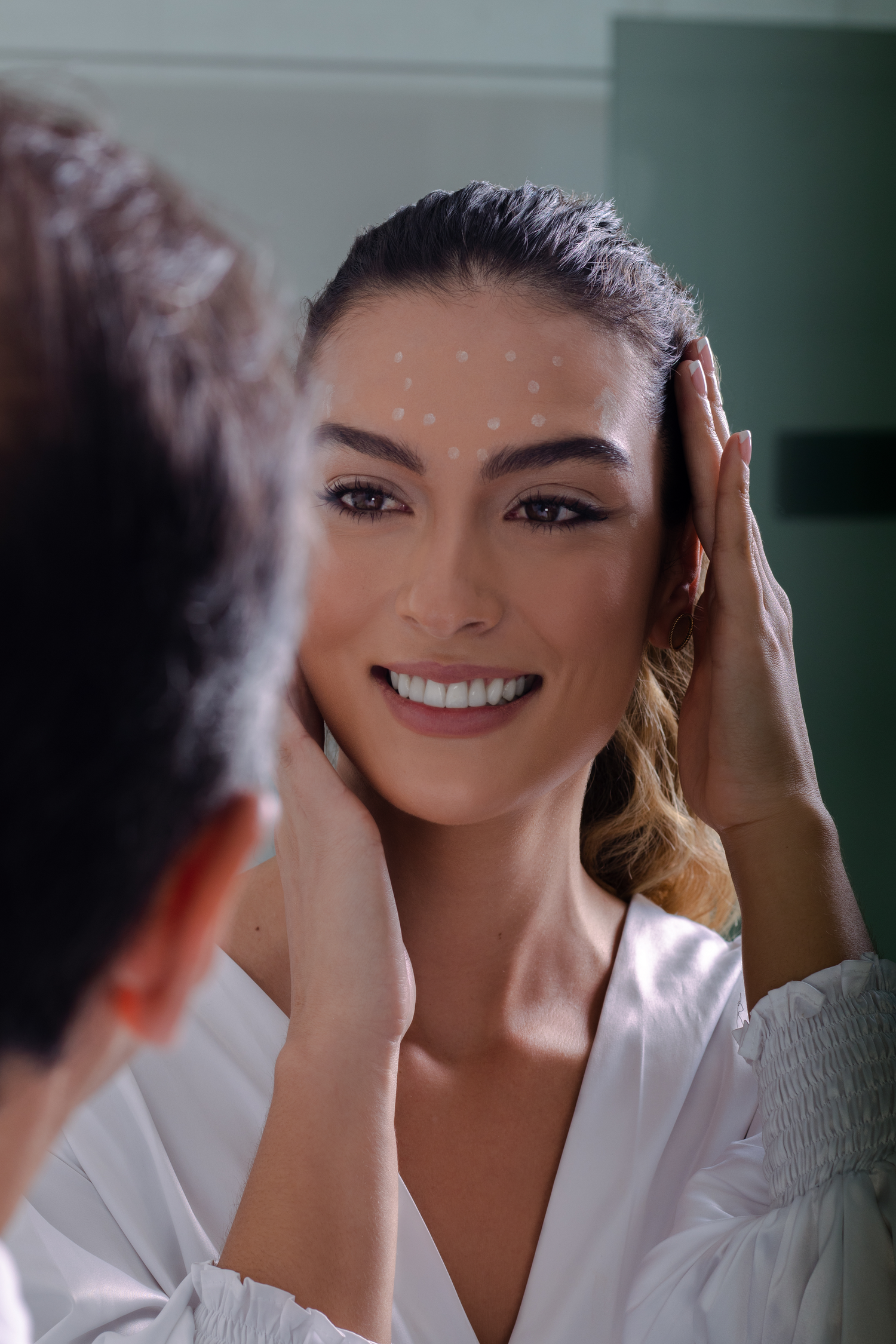 Patient smiling while looking in mirror during a cosmetic consultation in a medical office setting.