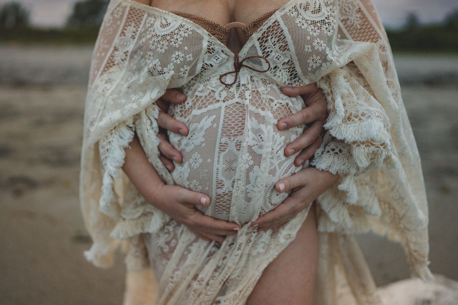 A pregnant woman in lace dress cradles her belly outdoors.
