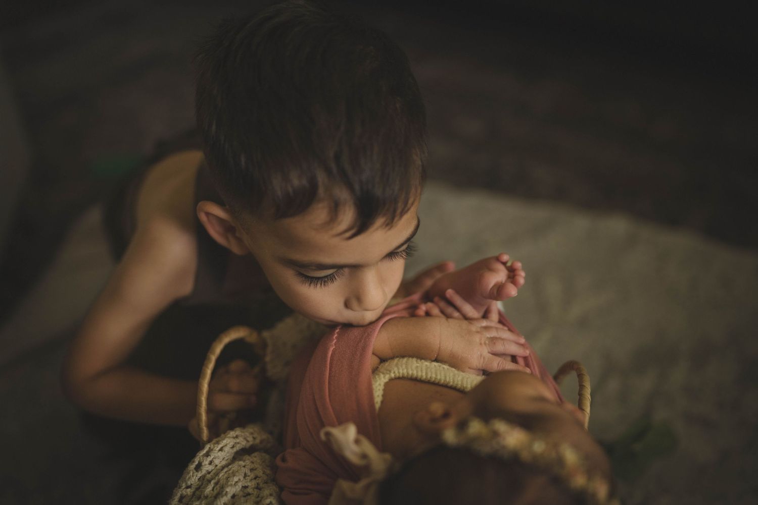 Child tenderly examining sleeping baby wrapped in soft fabric.