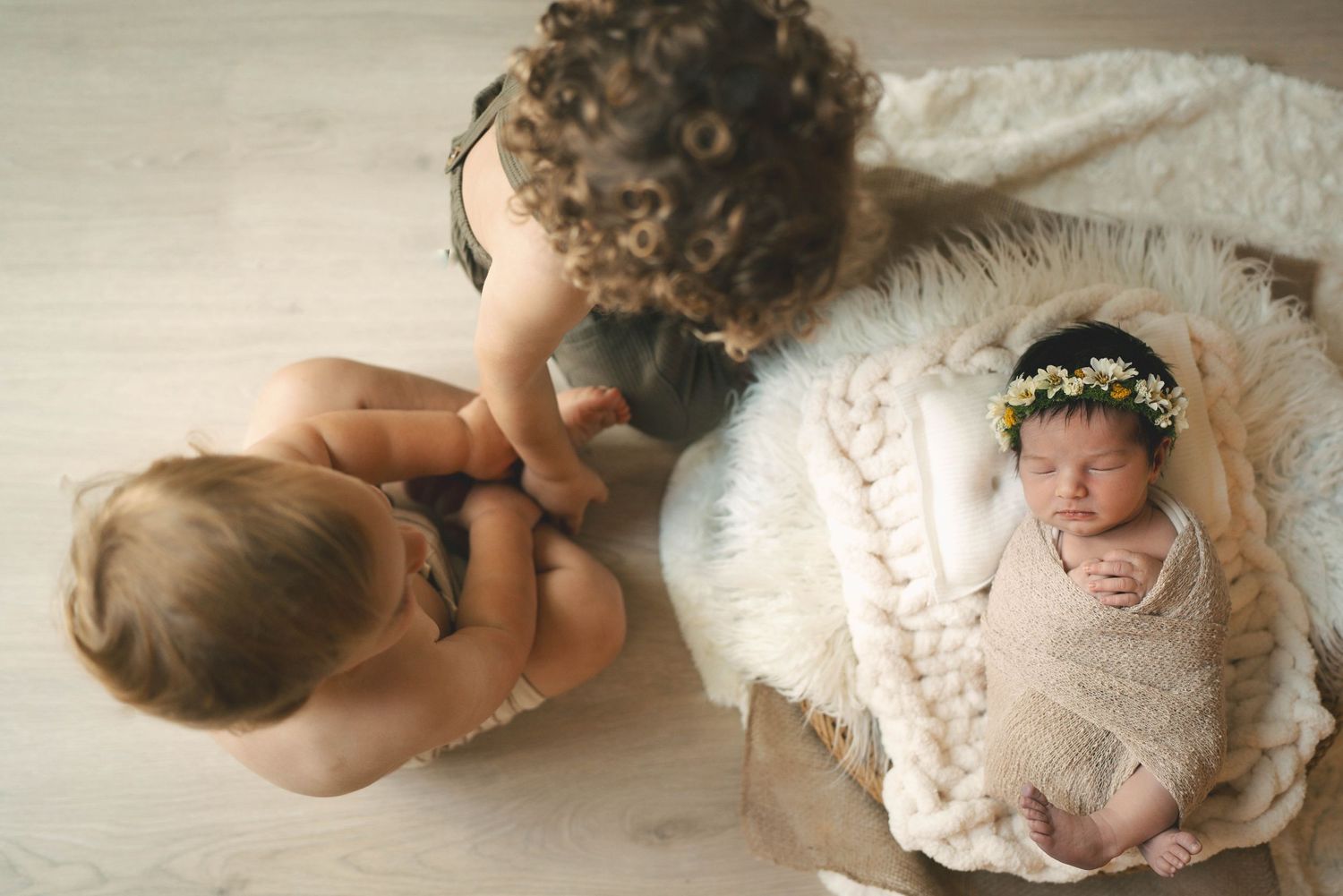 Two siblings looking at newborn baby in white basket on floor.