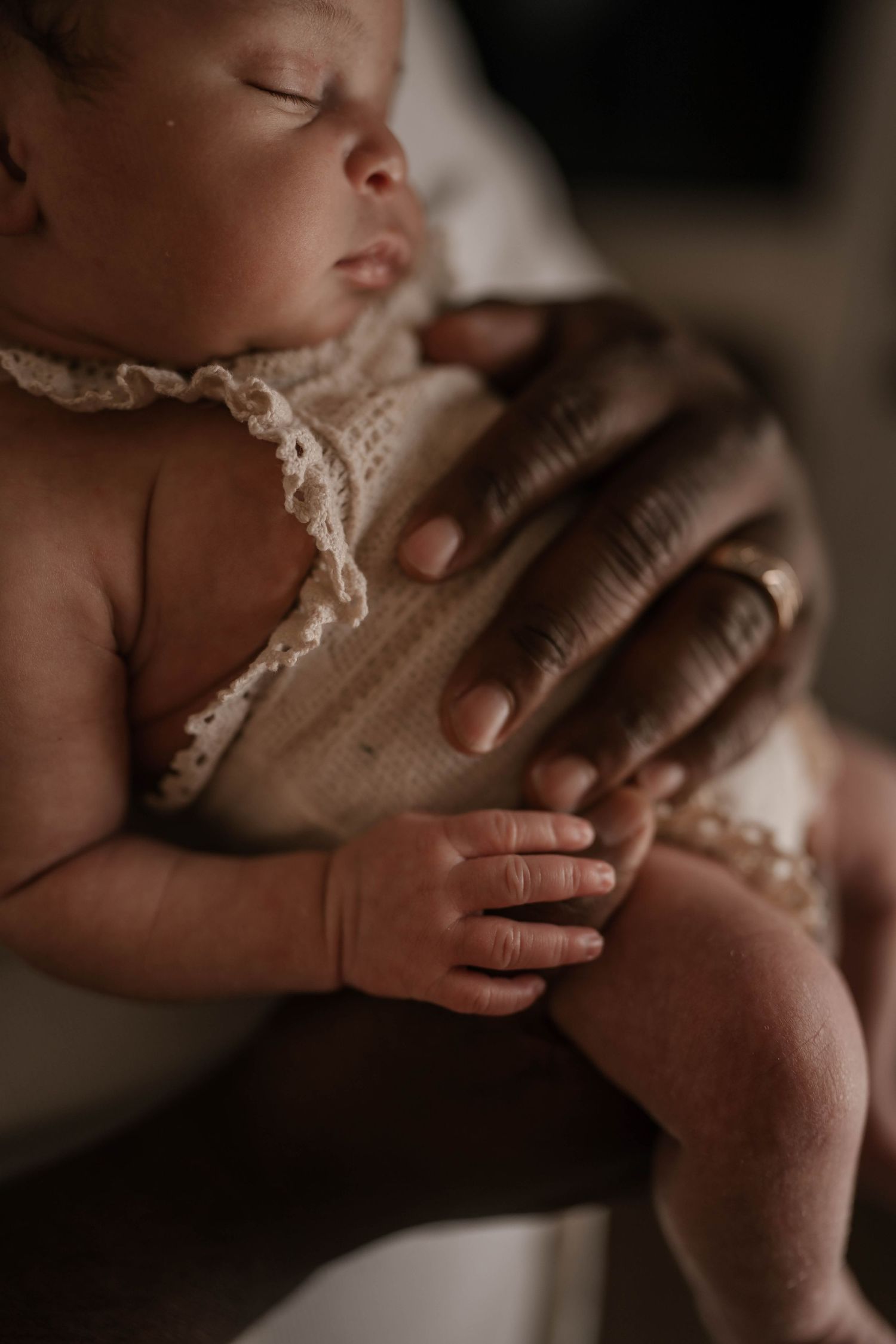 Close-up of sleeping newborn in lace trim being gently held.