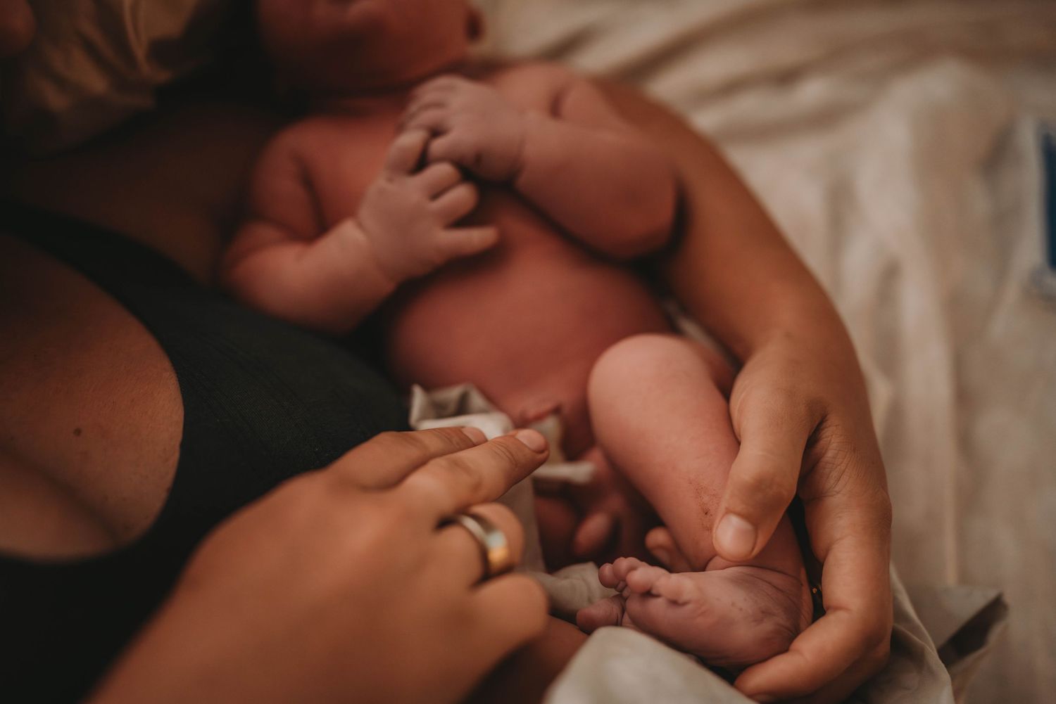 Gentle hands cradle tiny newborn against soft fabric in intimate moment.
