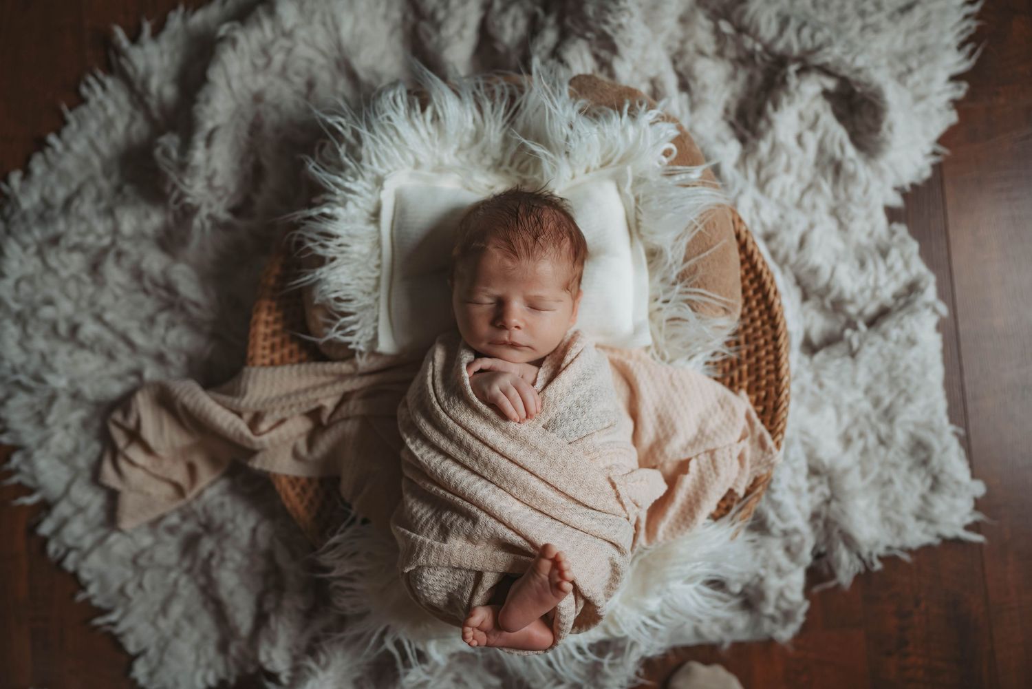 Newborn baby sleeping in basket surrounded by white fluffy rug.