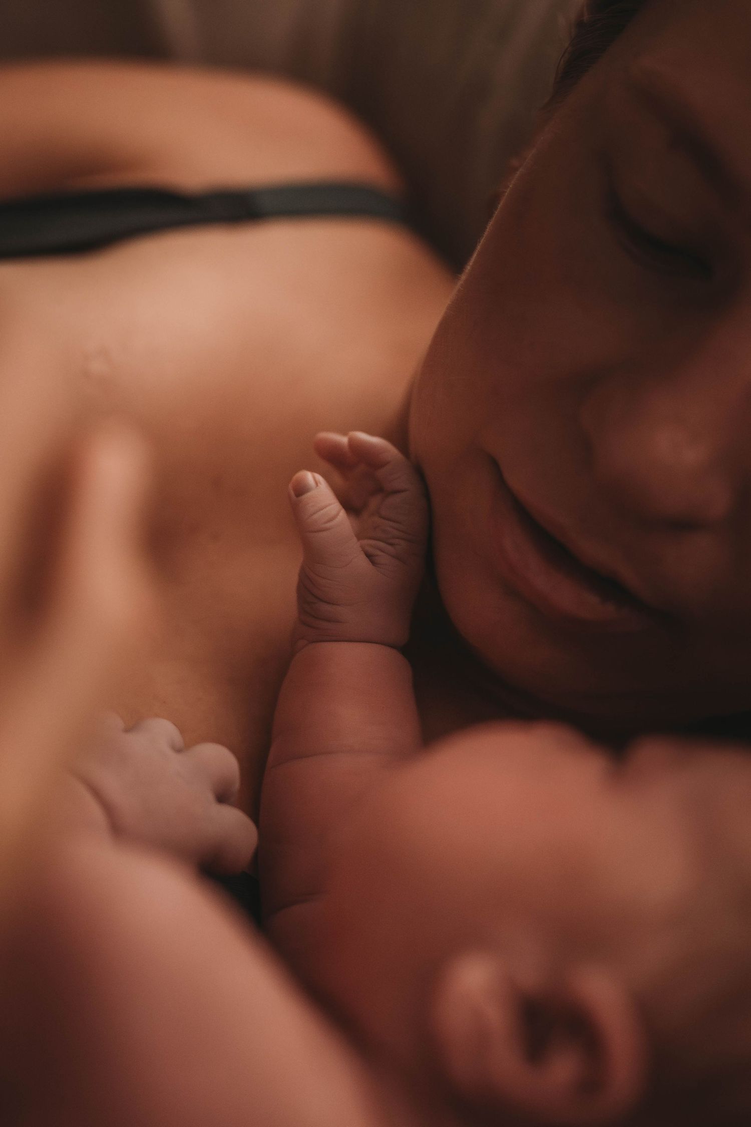 A tender close-up of an infant's small hand touching their face while resting in what appears to be a nurturing embrace.