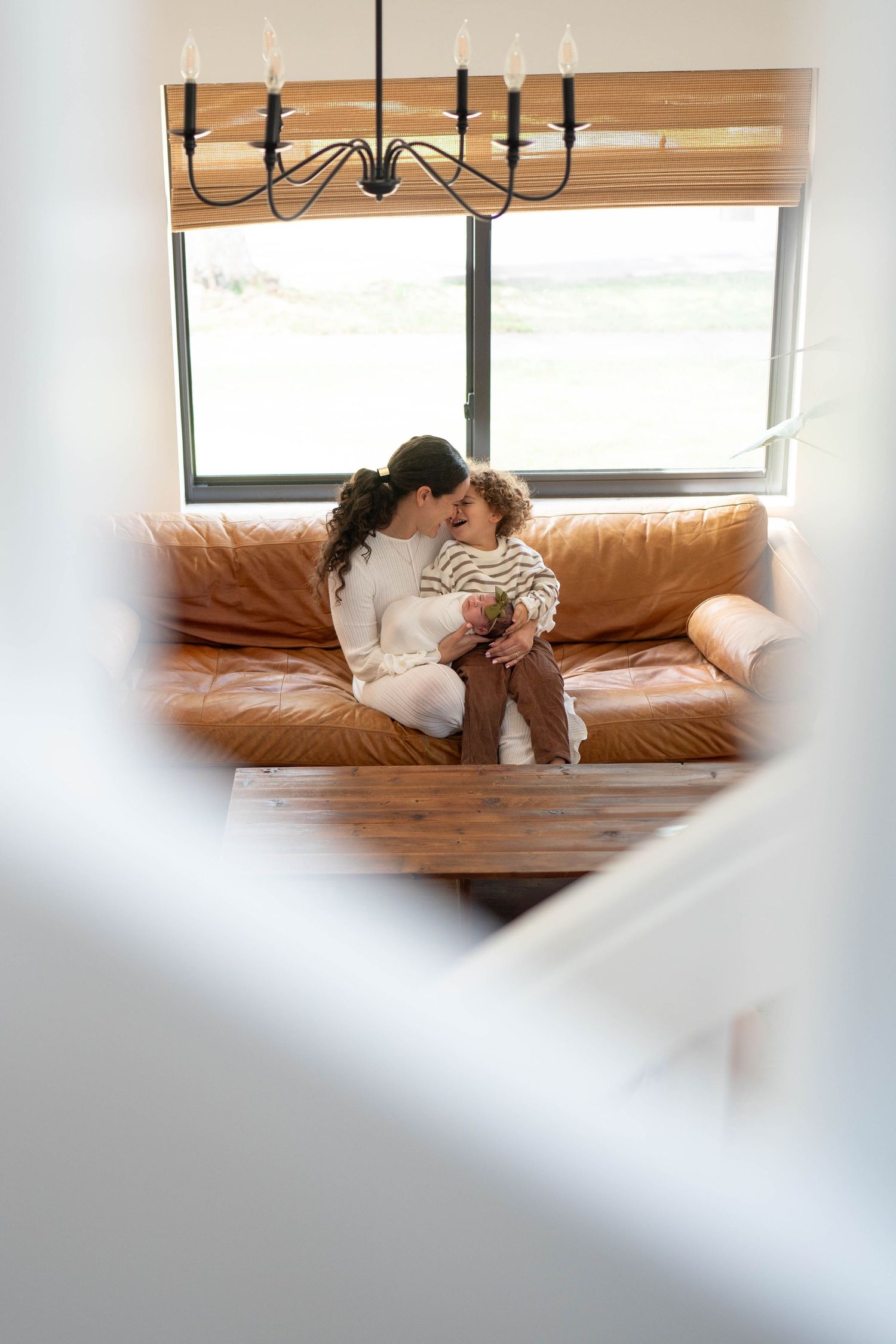An intimate family moment on a tan leather couch under a modern chandelier.