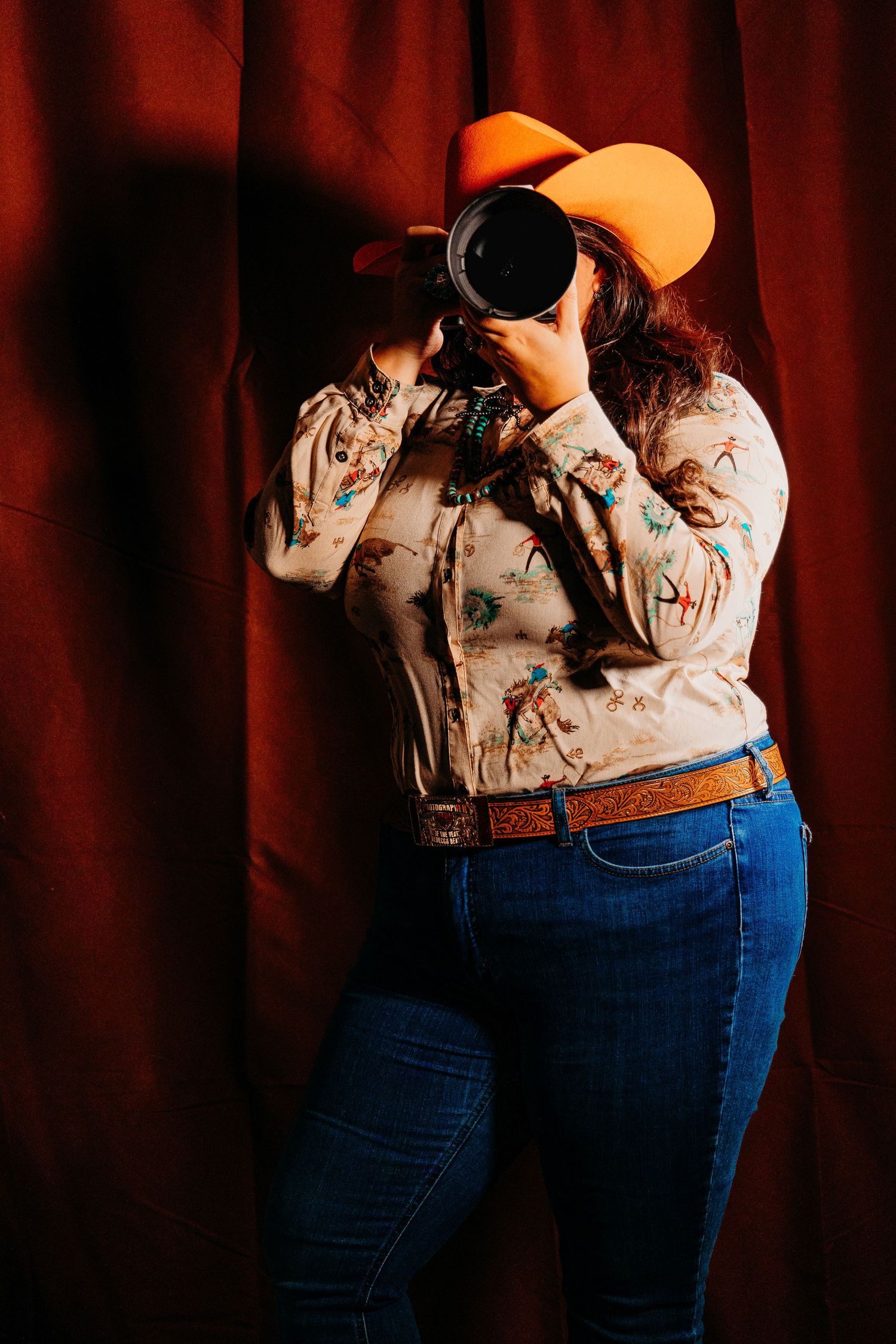 Western Portrait Photographer wearing Cavender's shirt, jeans and orange cowboy hat holds professional camera in Kentucky