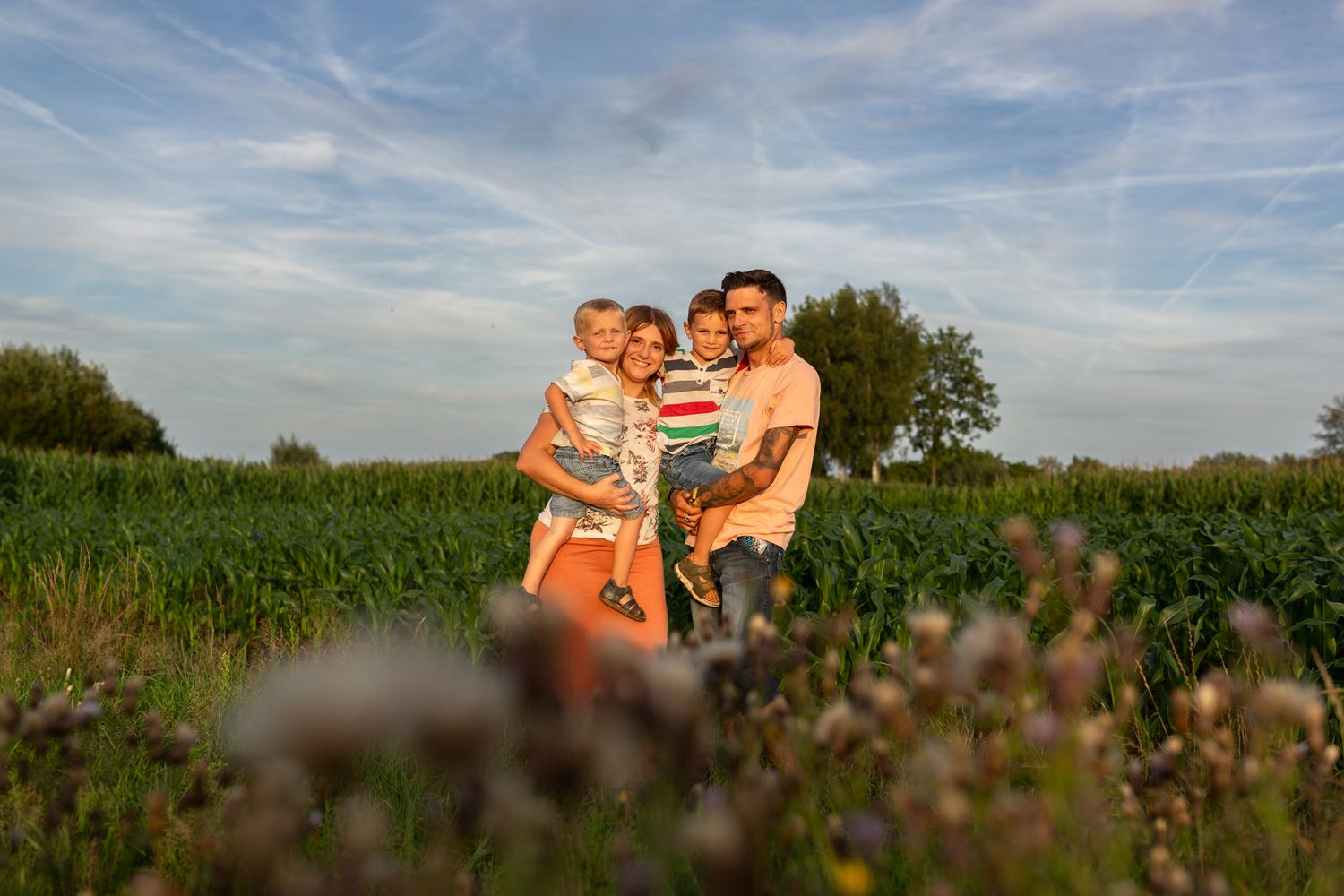 Family enjoying sunset together in wildflower field under blue sky.