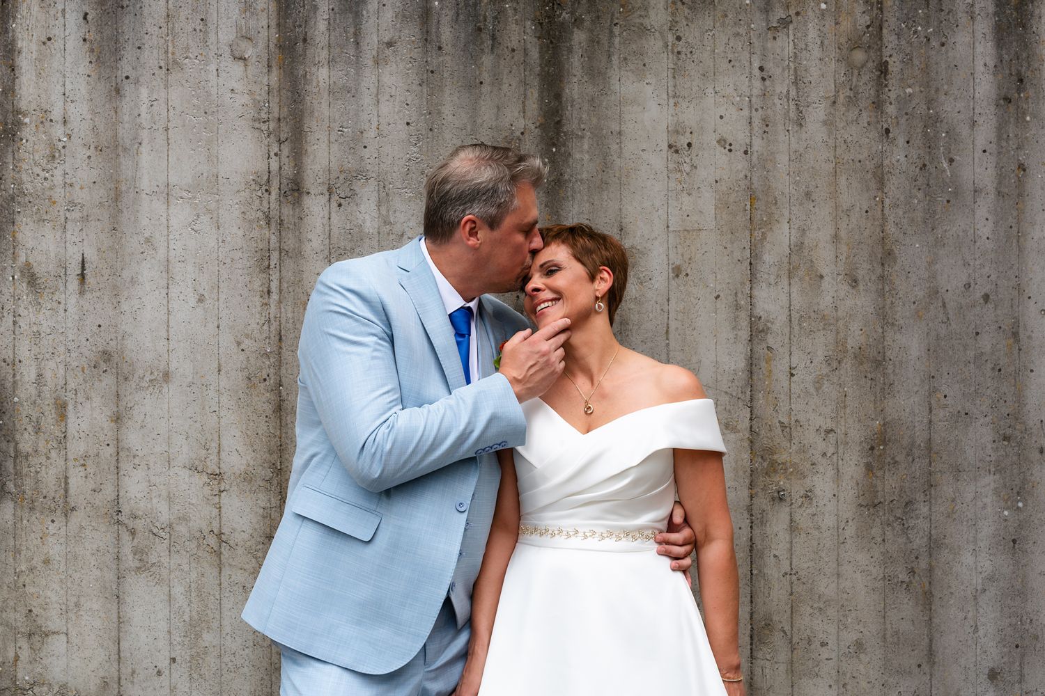 Intimate wedding portrait against concrete wall with couple in formal attire.
