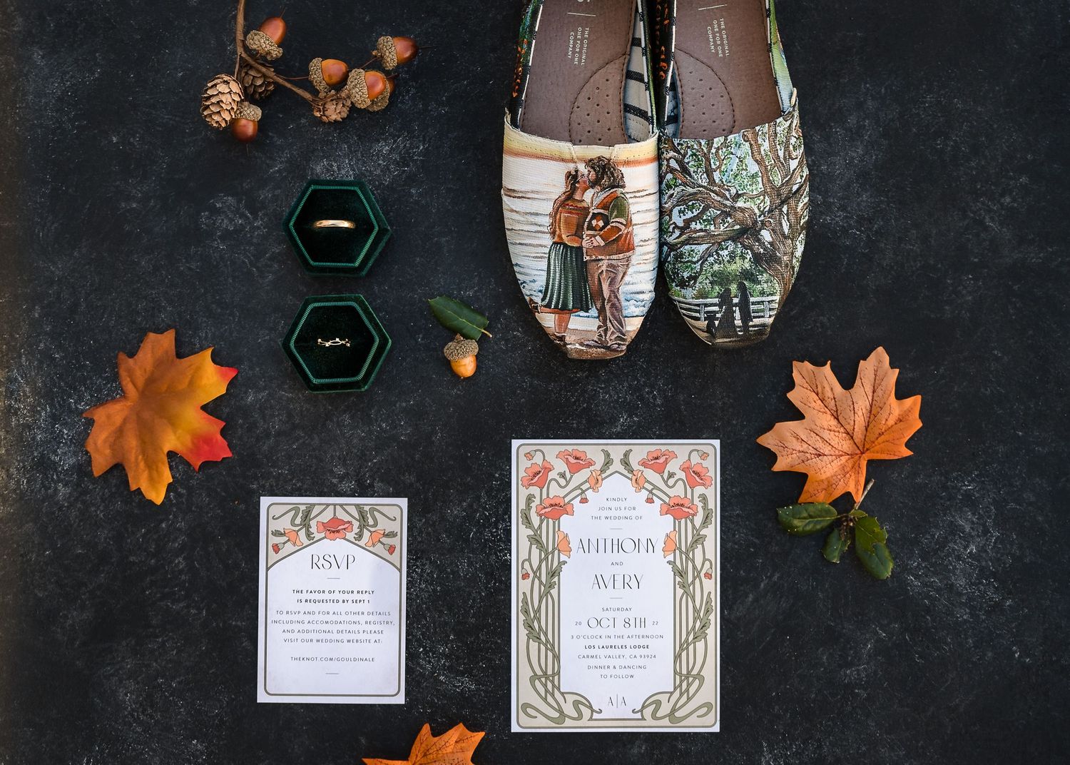 Overhead view of wedding invitations with autumn leaves and decorative elements arranged on dark textured background.