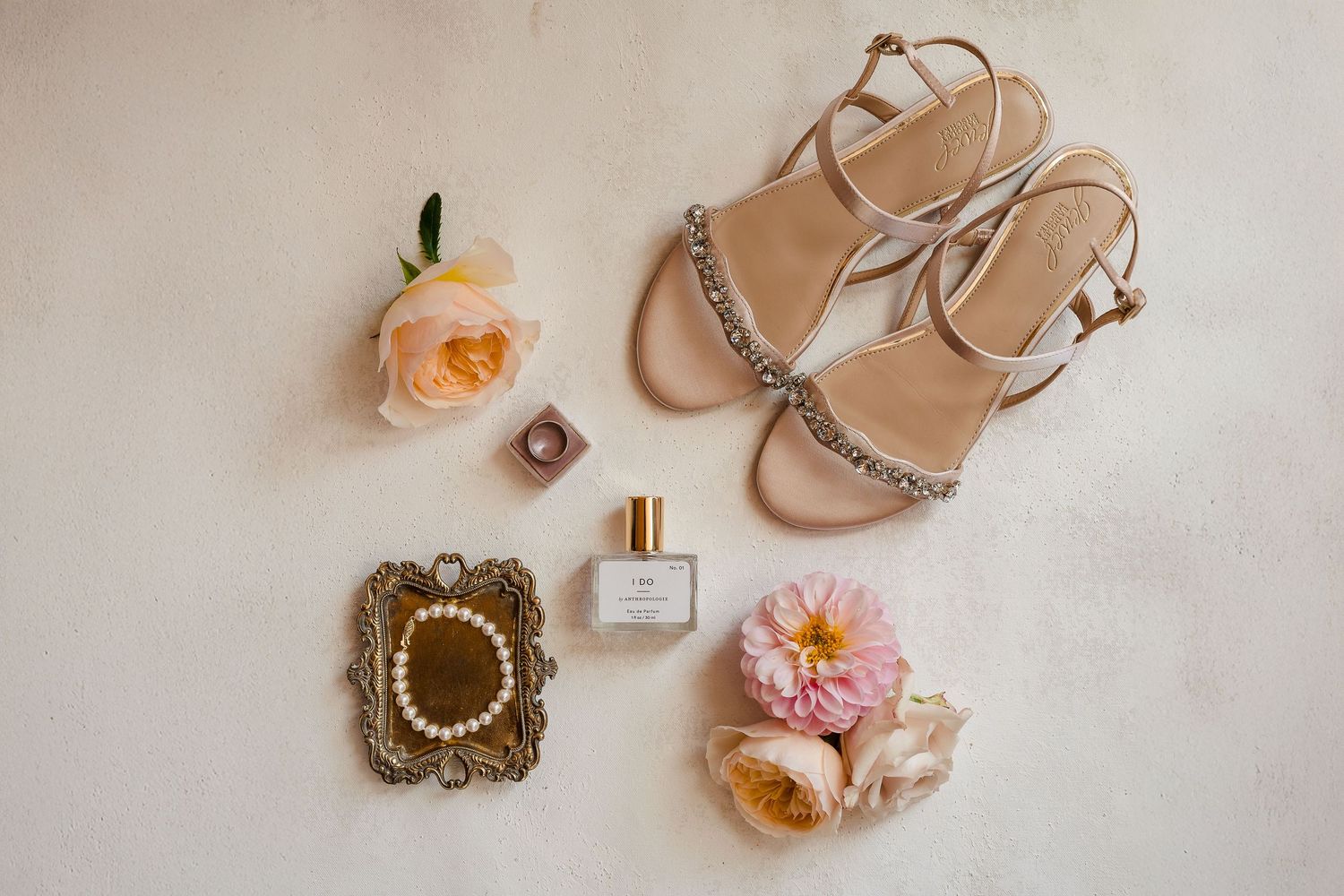 Elegant nude wedding heels with delicate pearl details arranged with perfume bottle and floral accessories.
