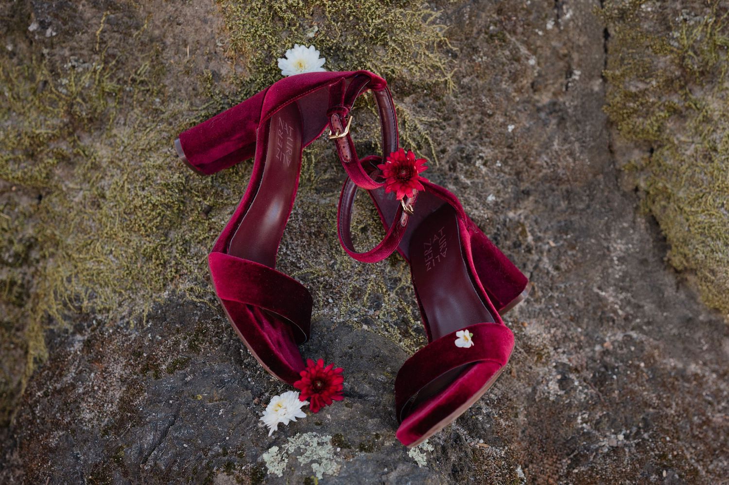 A sequence of burgundy velvet high heel shoes arranged on a textured stone surface.