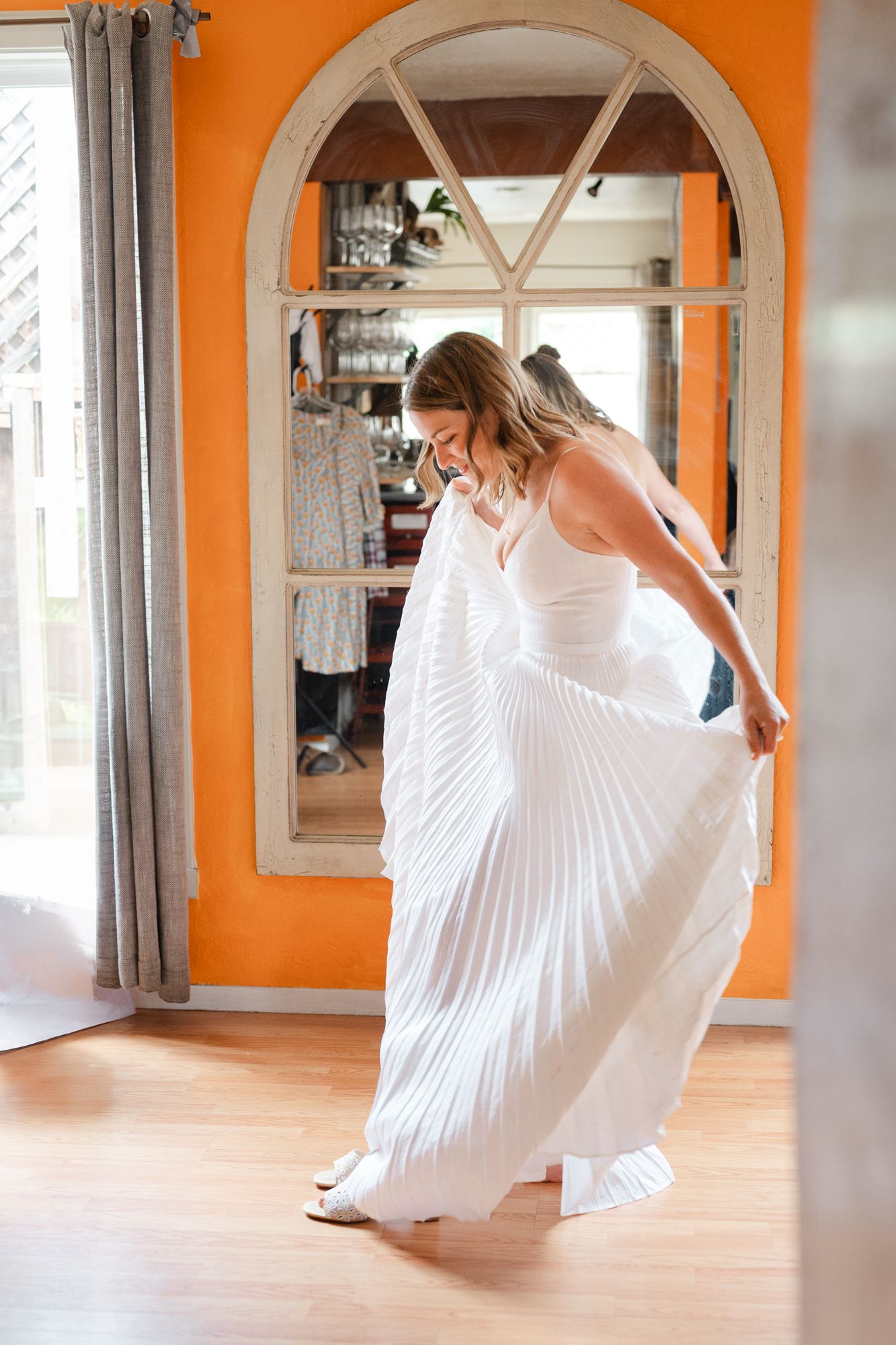 A figure in a flowing white pleated dress twirls gracefully in an orange-walled hallway with arched doorways.