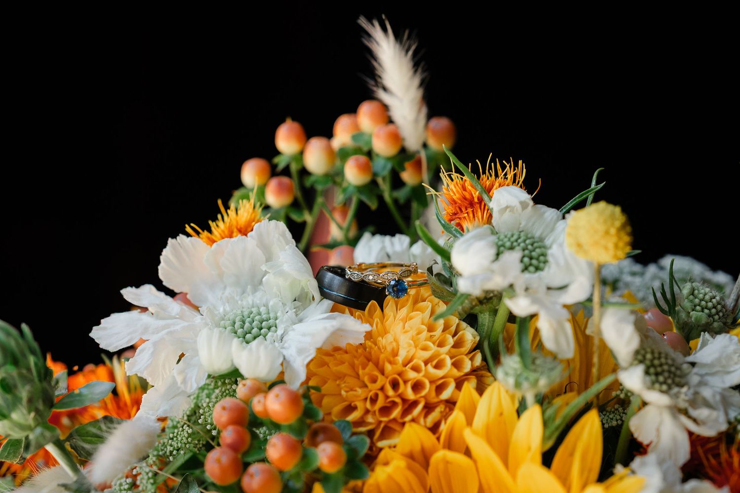 Vibrant floral arrangement featuring orange marigolds, white daisies, and green berries in a rustic garden setting.