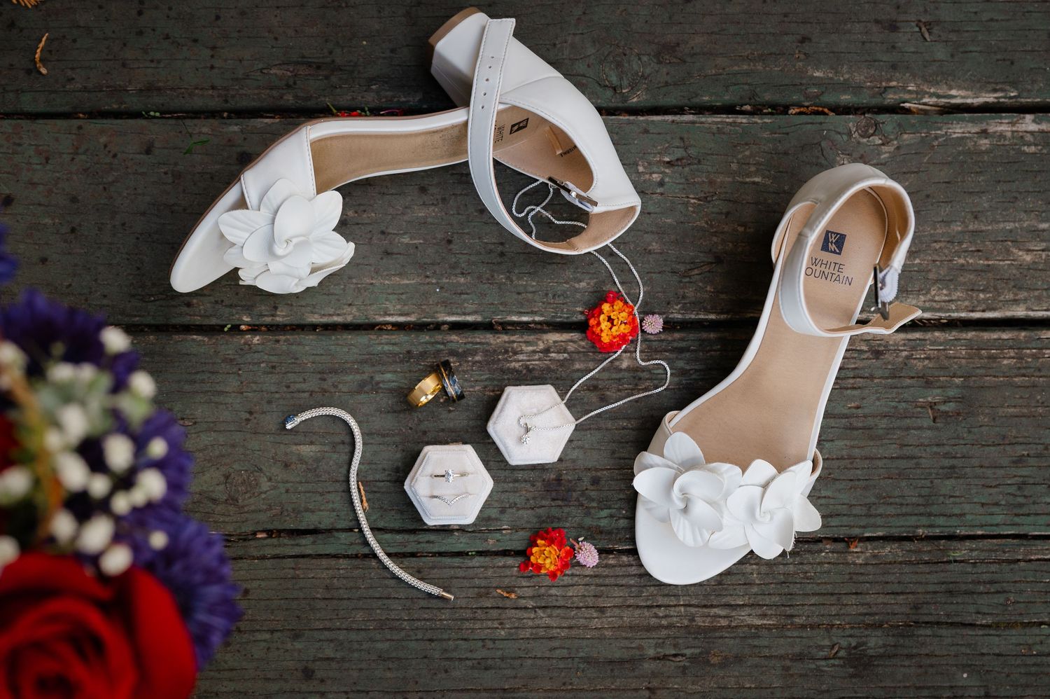 Wedding accessories including white shoes and delicate floral decorations arranged on rustic wooden planks.