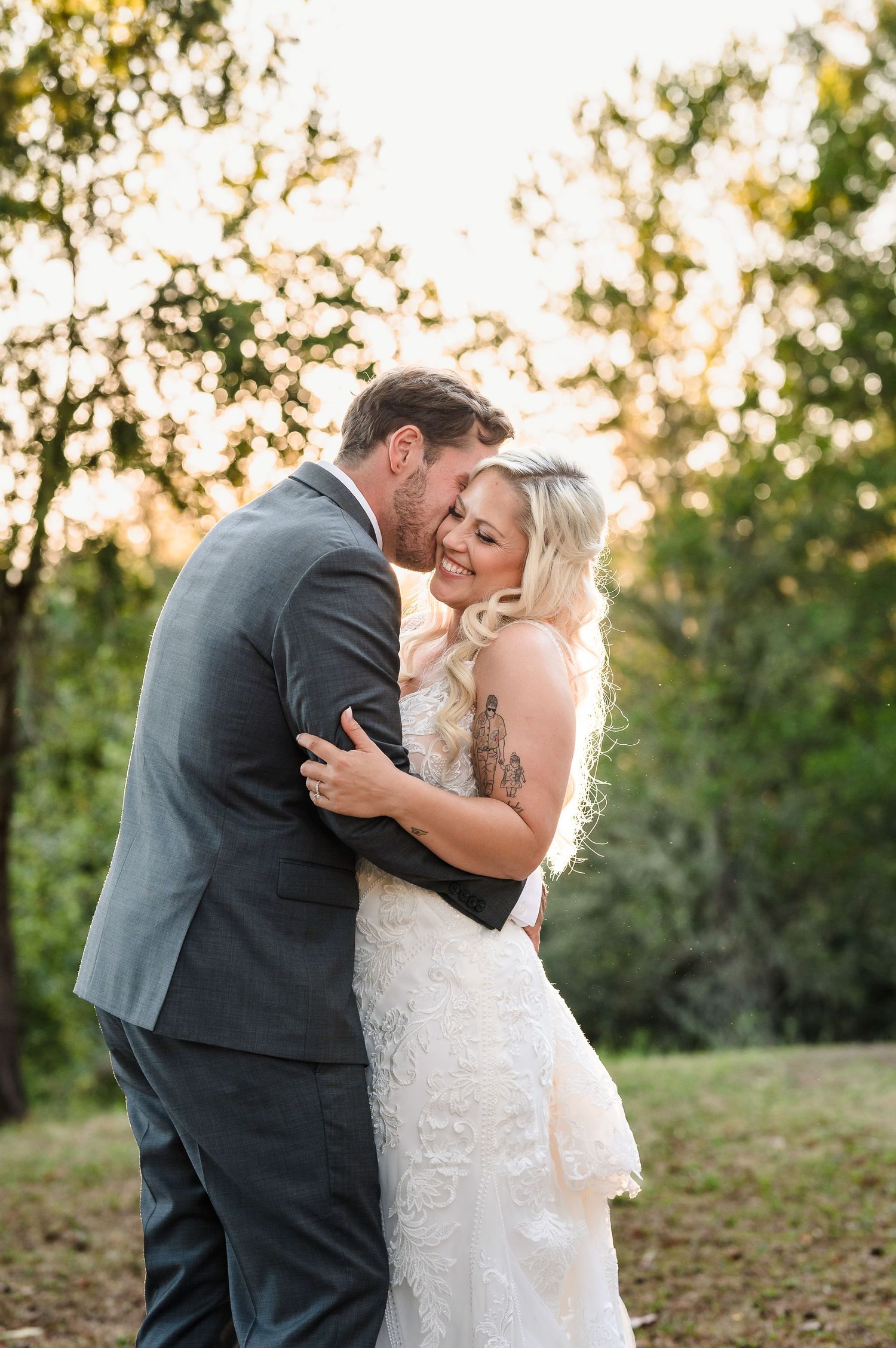 Bride and groom embrace during golden hour sunset at outdoor wedding venue with natural bokeh lighting.