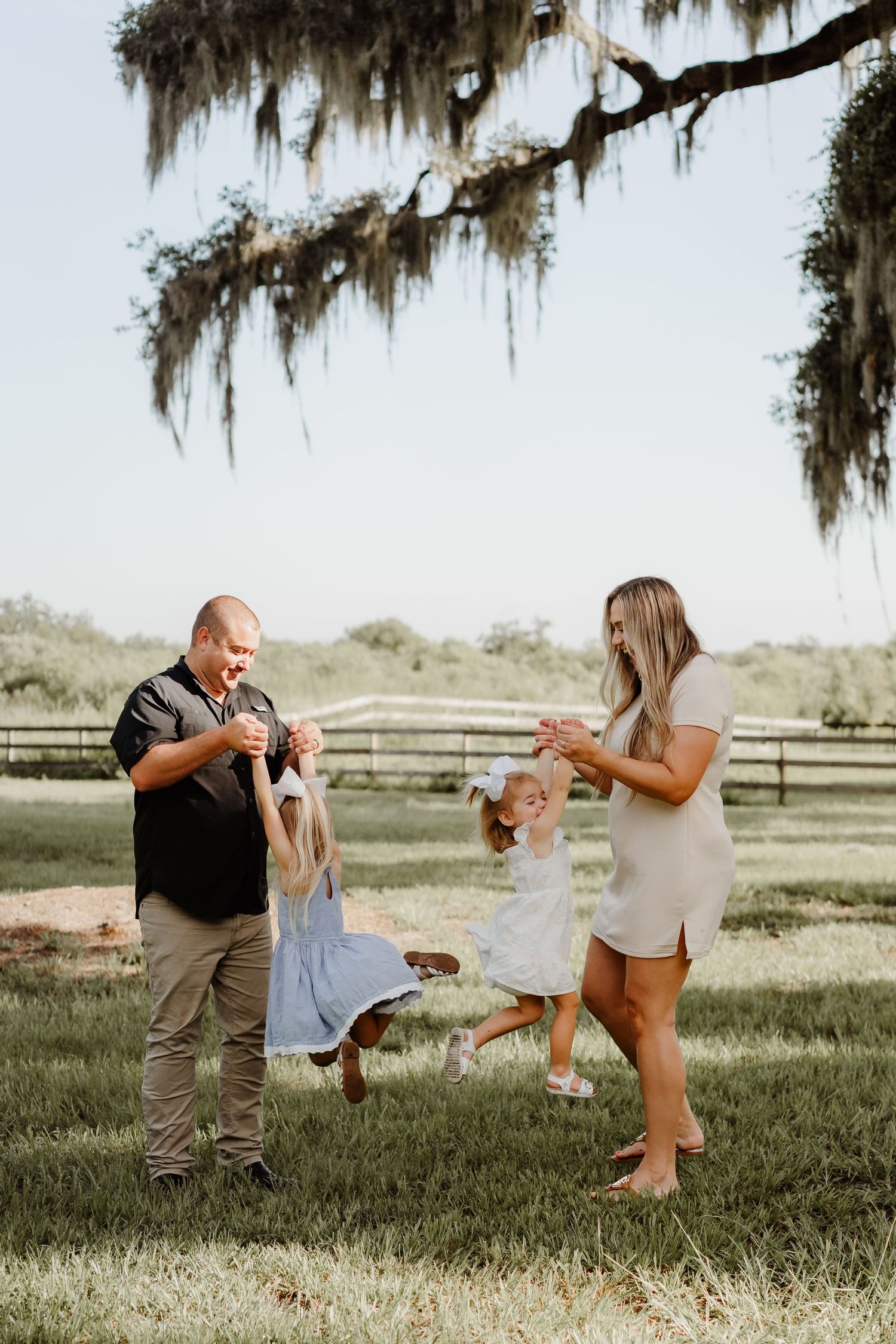 Family of four playing outdoors on green grass under Spanish moss-draped oak tree on a sunny day.