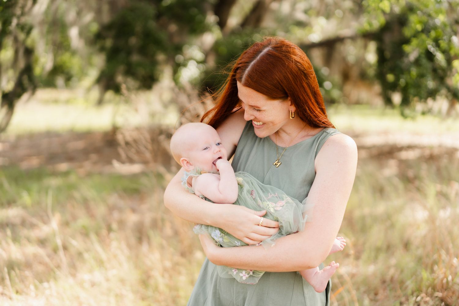 A tender moment between parent and baby outdoors in soft natural lighting with trees in the background.