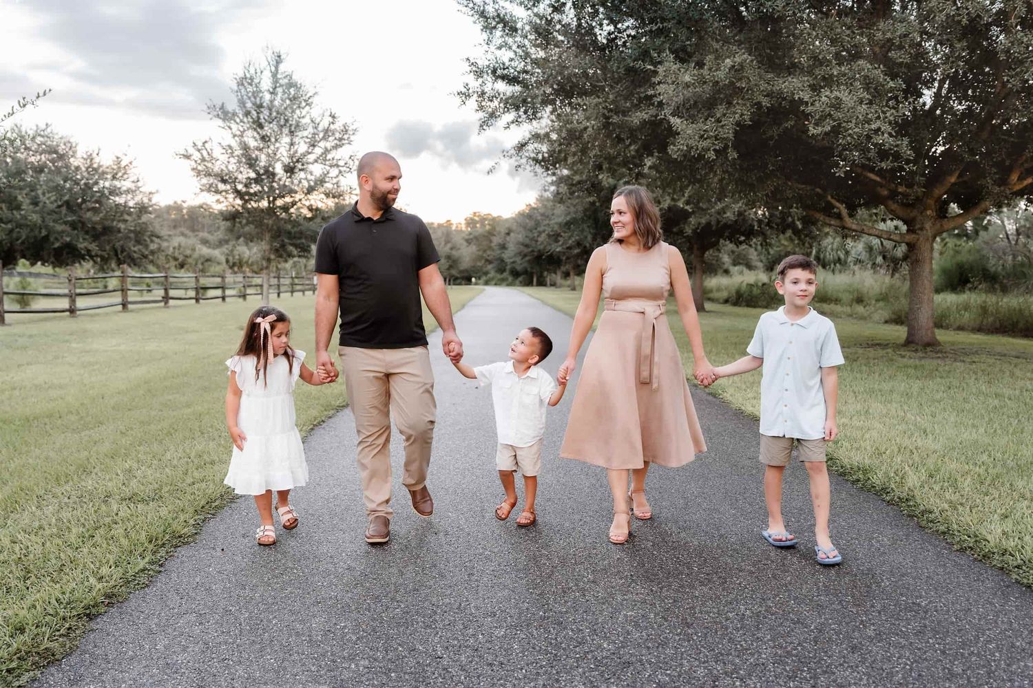 Family of five walking hand-in-hand on a tree-lined path during a golden hour outdoor photo session.