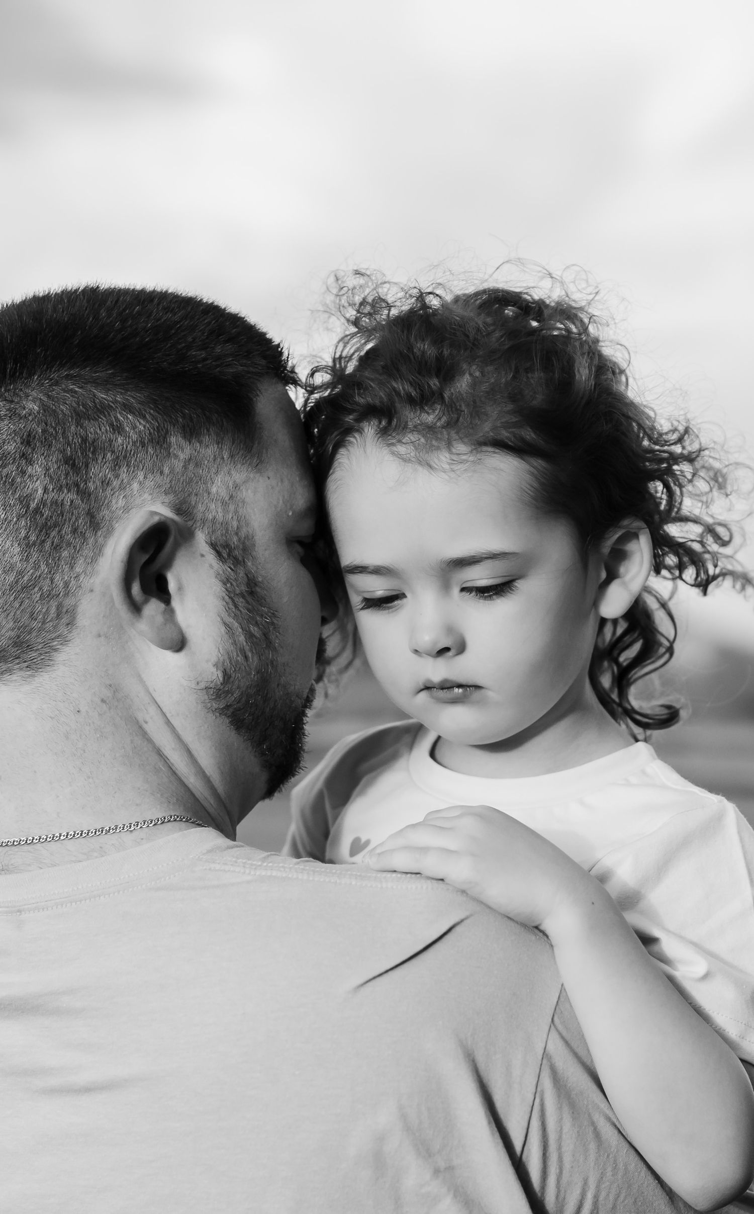 Tender black and white portrait of father holding young curly-haired child close.