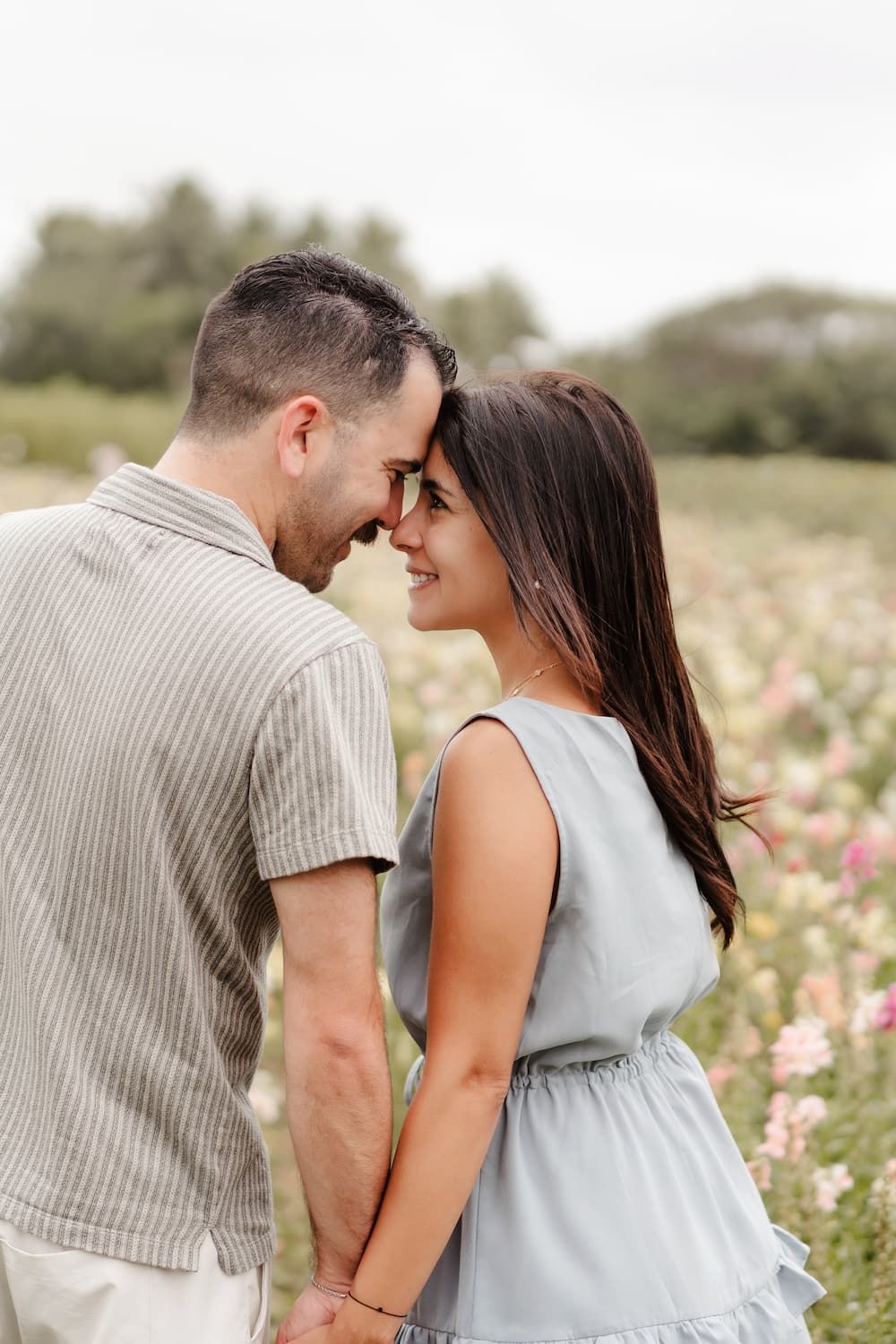 A romantic couple embraces in a wildflower meadow wearing coordinated neutral outfits on a sunny afternoon.