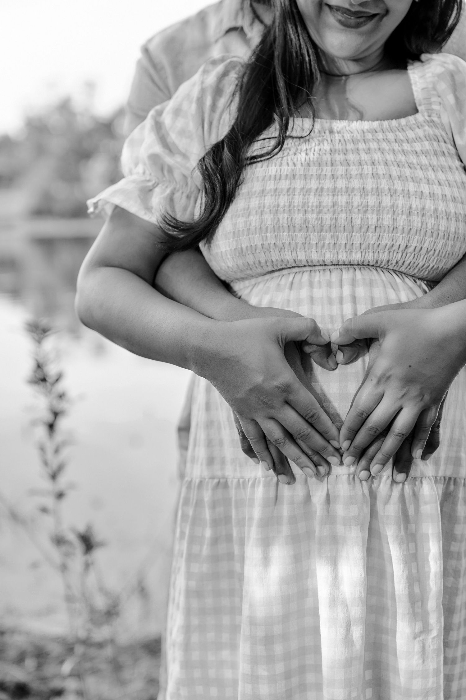 Black and white maternity photo series showing a woman's pregnant belly in a white gingham dress.