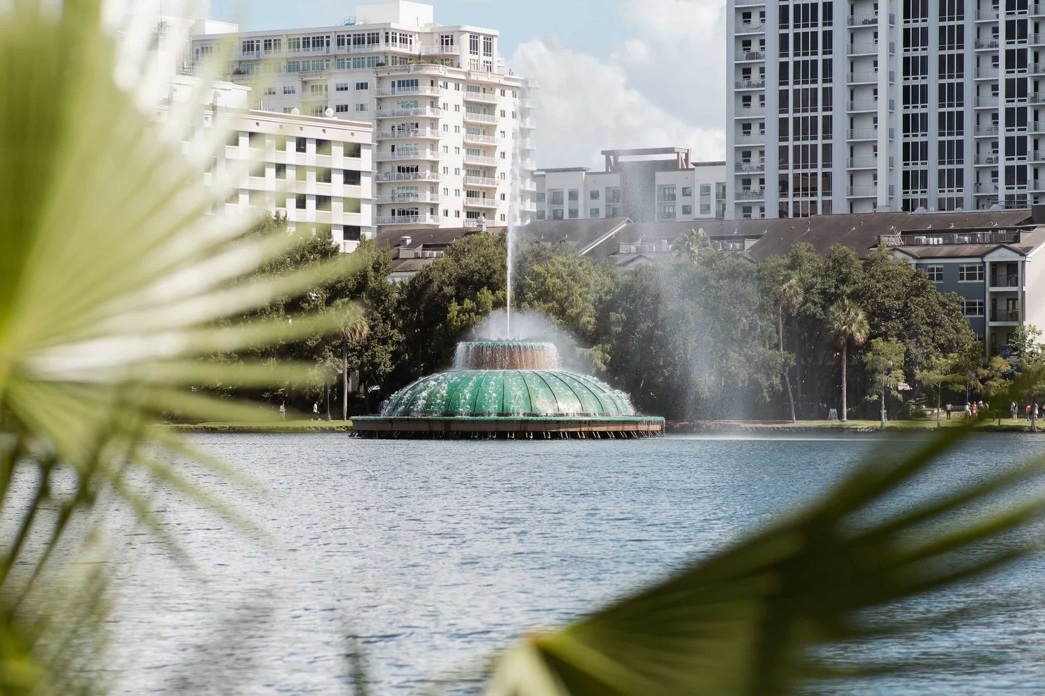 Iconic green fountain on Lake Eola in Orlando, Florida, surrounded by lush trees and modern city buildings.