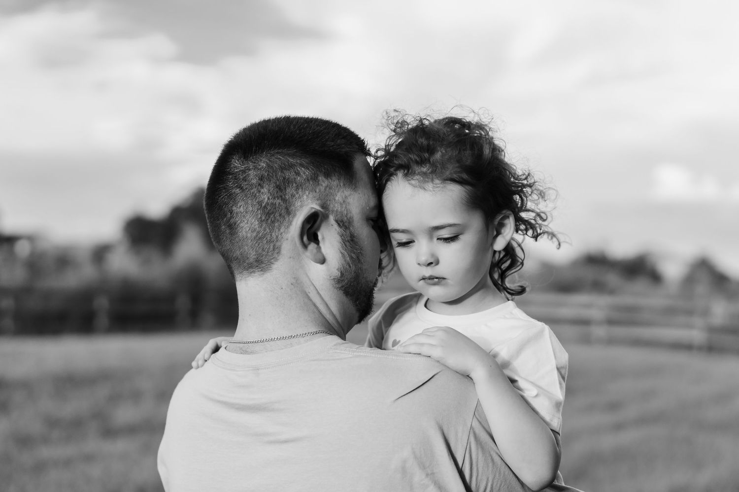 Black and white photo of a father tenderly holding his young curly-haired daughter outdoors.