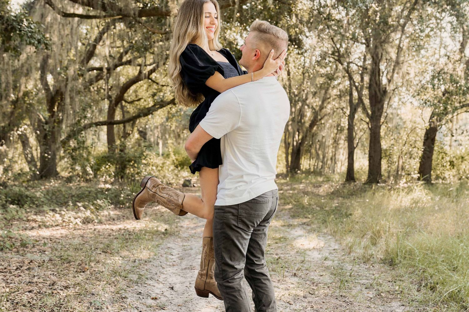 A couple embraces in a romantic outdoor photoshoot among sunlit trees in a natural wooded setting.