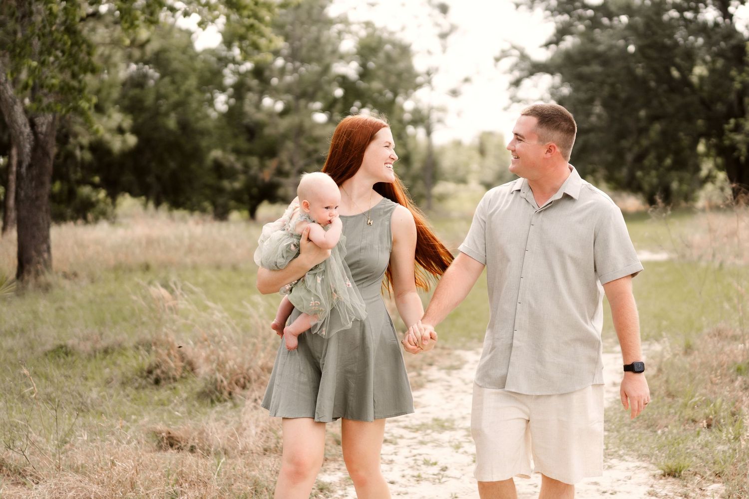 A couple walks hand in hand through a scenic meadow path wearing coordinated neutral-toned outfits.