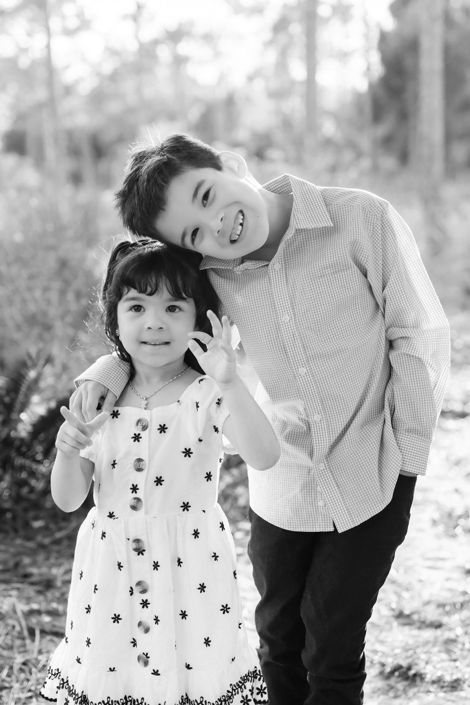 A black and white portrait of two children outdoors, one wearing a patterned dress and another in a button-down shirt.