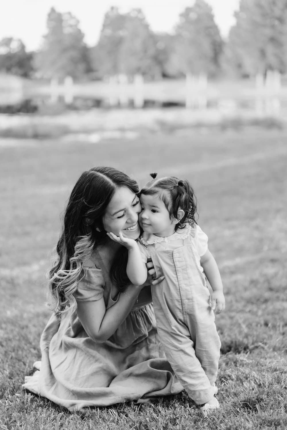 Black and white photo of a tender moment shared between parent and child sitting together on grass outdoors.
