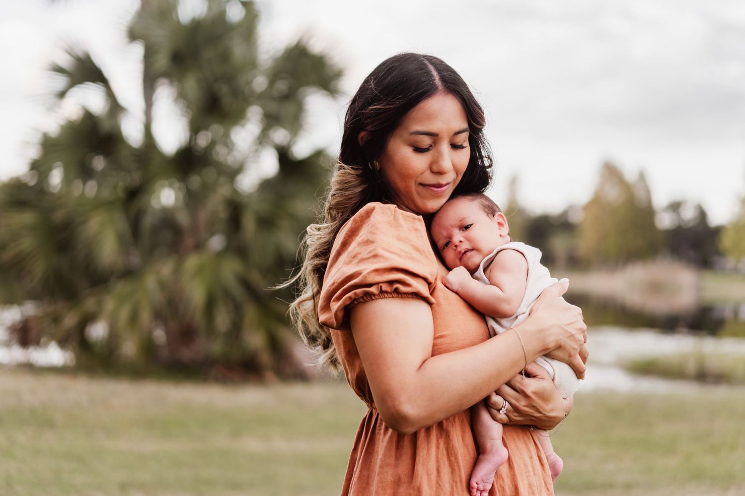 A mother in a peach dress holds and comforts her baby in a series of tender outdoor portraits.