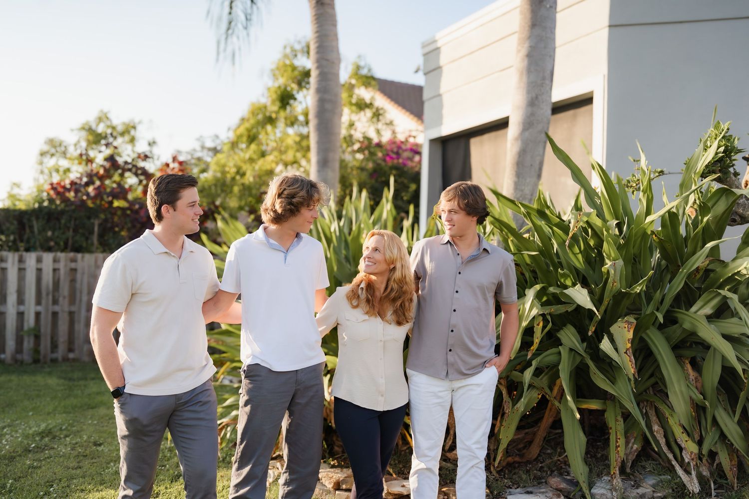 A group walks together outdoors wearing casual white and neutral clothing against a backdrop of tropical foliage.
