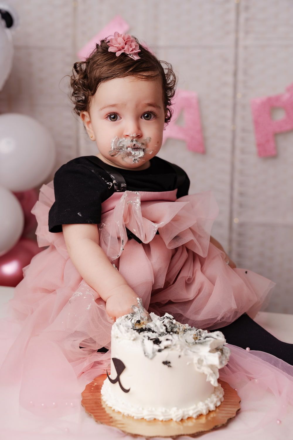 Messy cake smash photo with pink tulle dress and white frosting on face during first birthday celebration.
