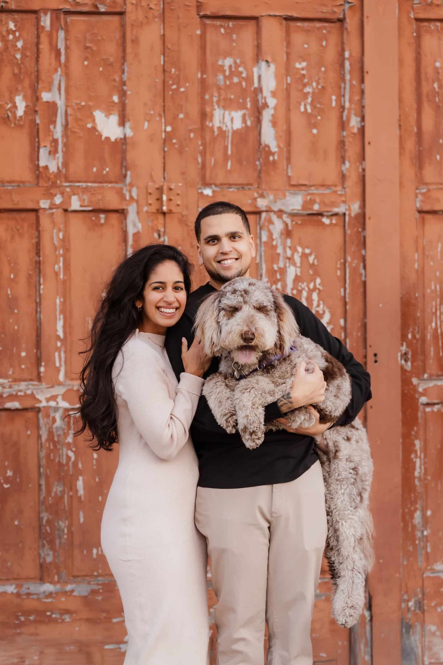 Family poses with their fluffy gray dog against a rustic orange metal wall background.