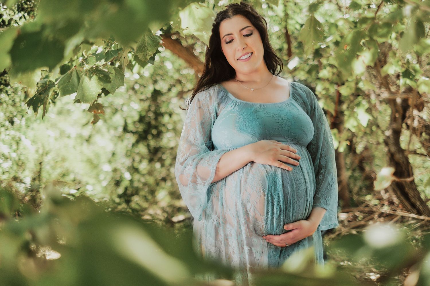 Maternity photoshoot in a blooming spring orchard with soft natural lighting and white blossoms.