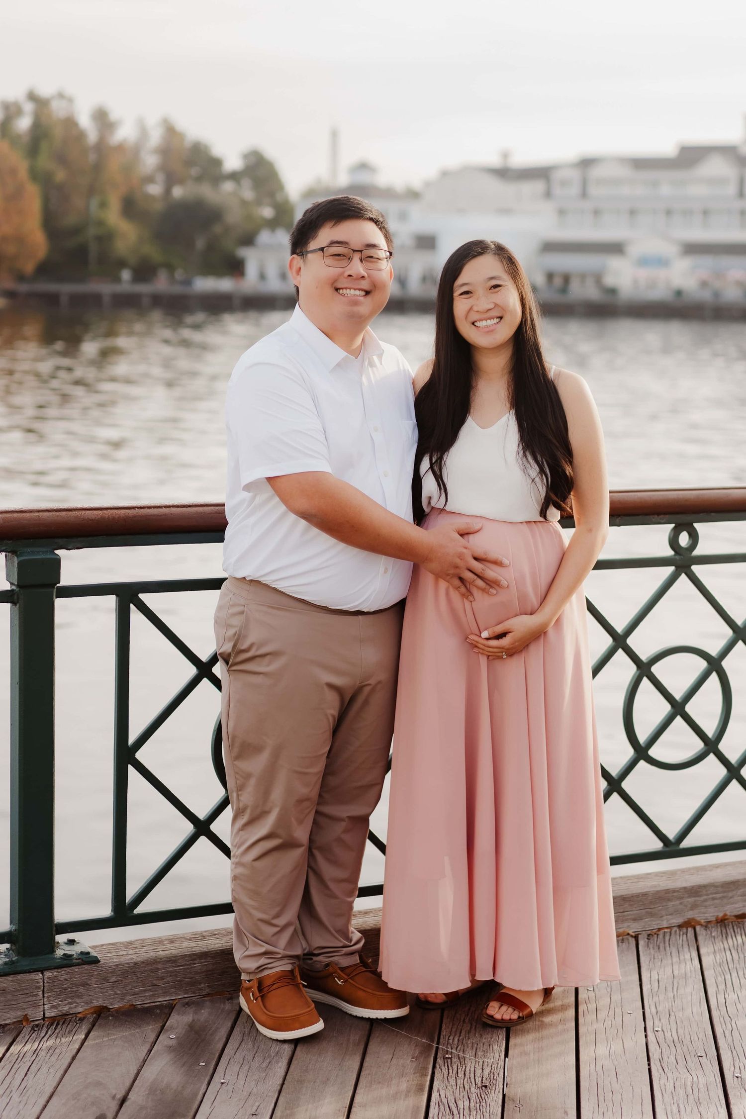A couple sits together on a wooden boardwalk by the water during an outdoor engagement photoshoot.