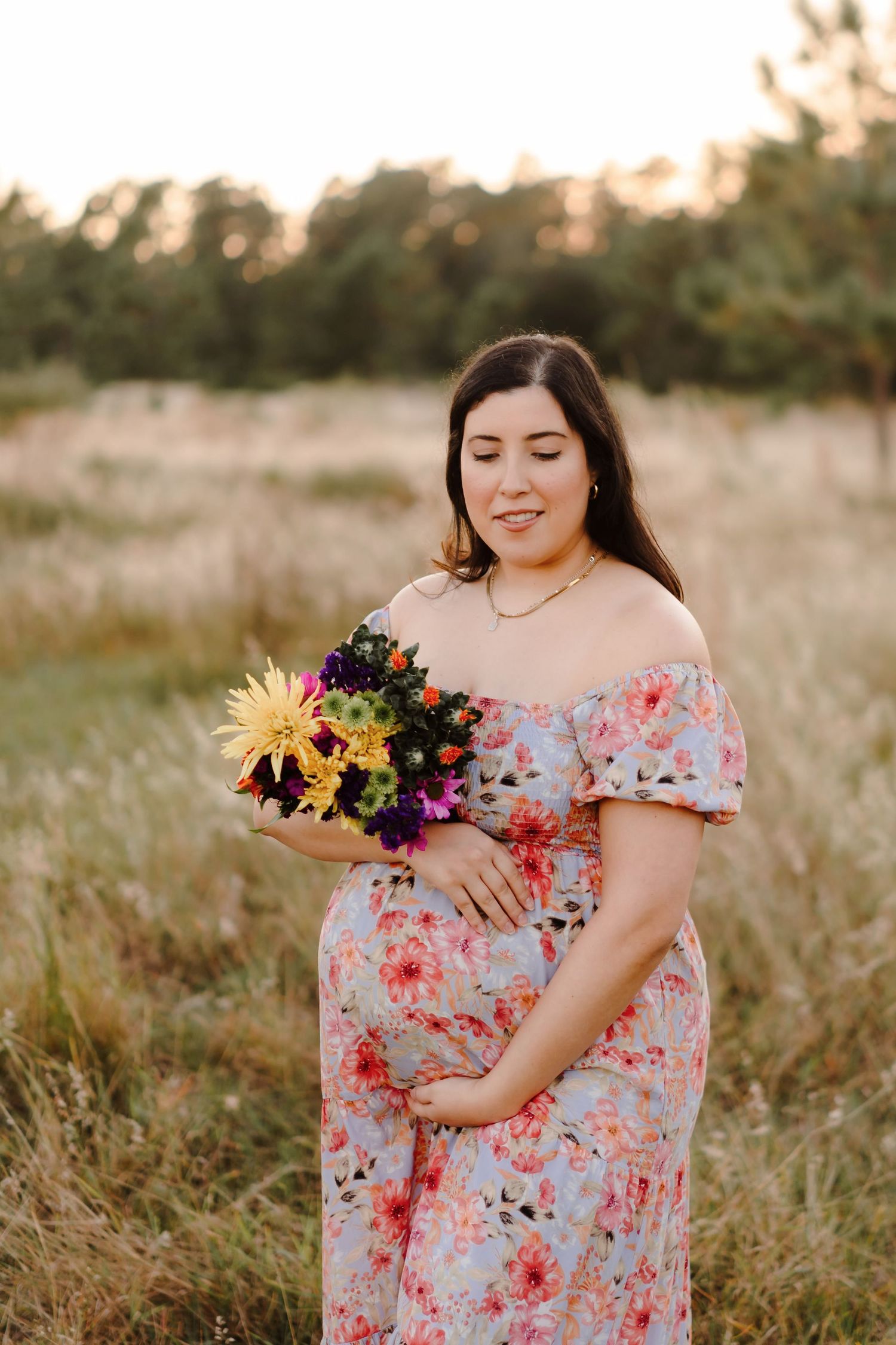A floral dress-clad figure poses gracefully in a sunlit meadow holding colorful wildflowers at sunset.