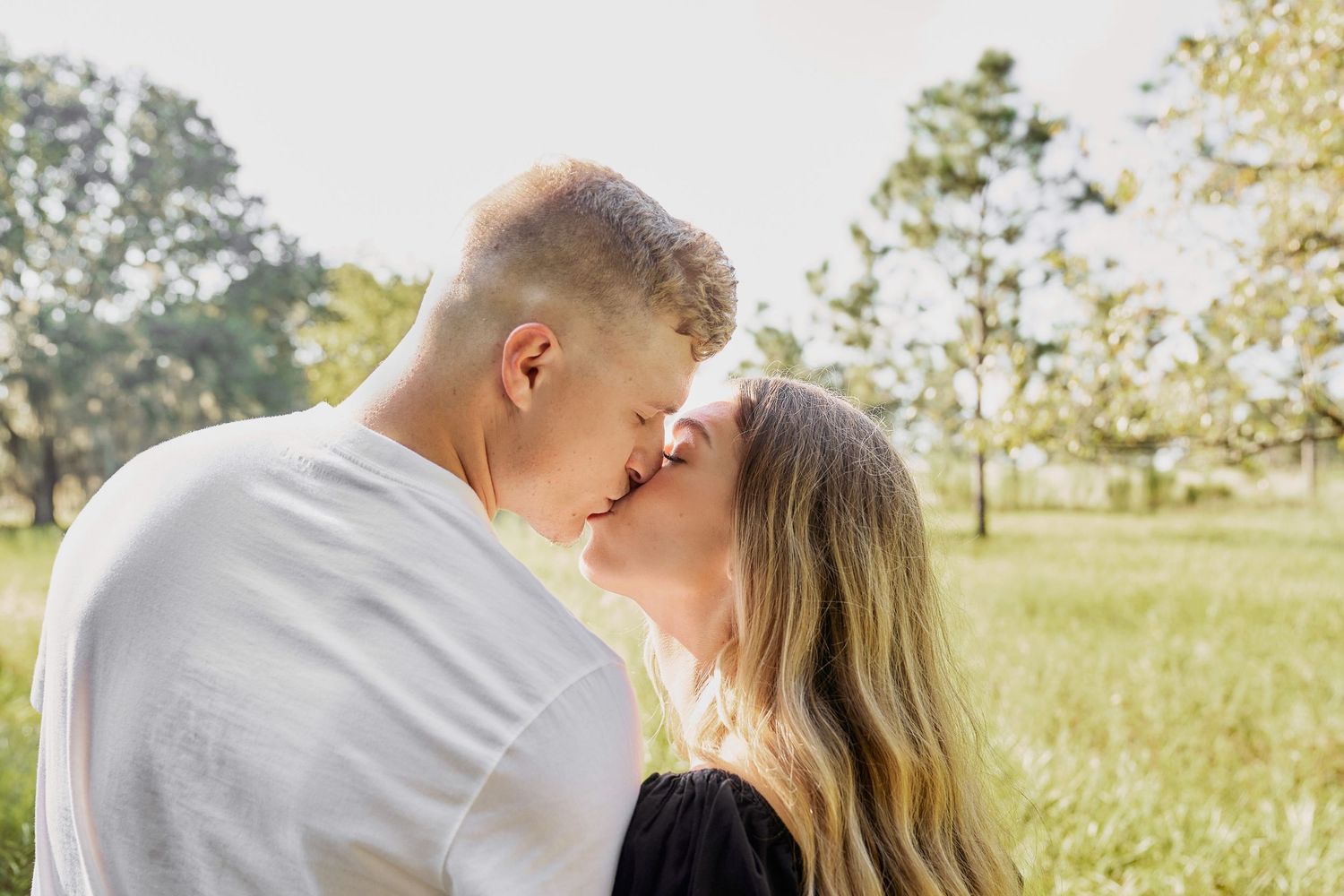 A romantic couple shares tender moments in a sunlit meadow during a golden hour photoshoot.