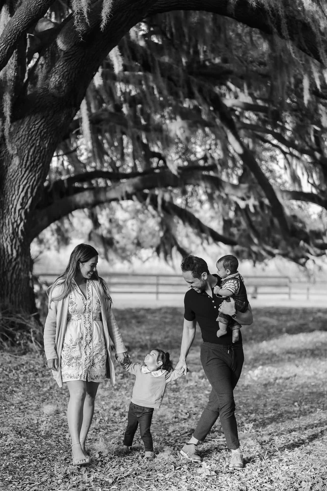 A black and white image of a family of four walking together in a wooded area.