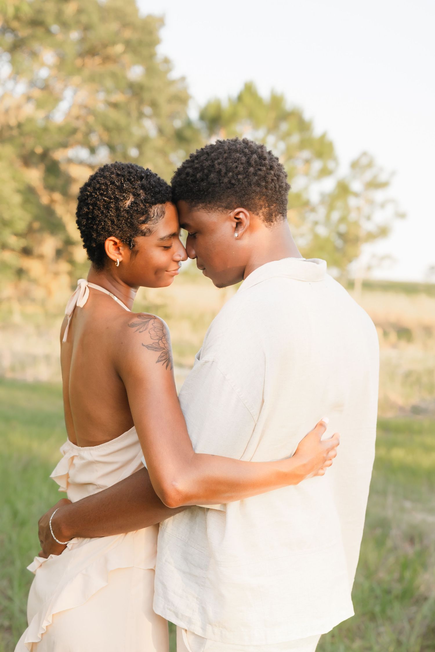 A romantic couple embraces in a golden sunlit field during a tender outdoor photo session.