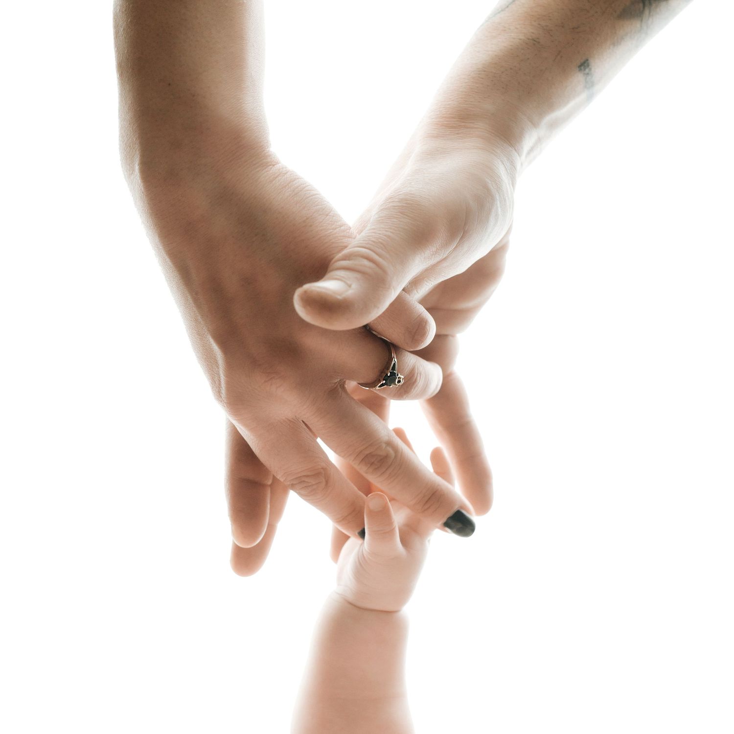 Close-up of parents and newborn baby hands stacked together, mother wearing elegant ring, on white background.